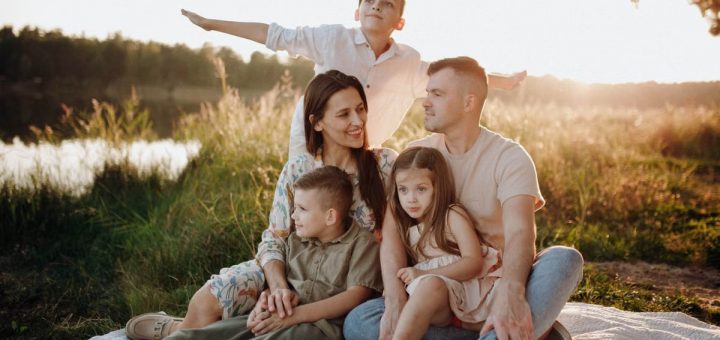 A family of five enjoying a serene picnic in a sunlit meadow during sunset.